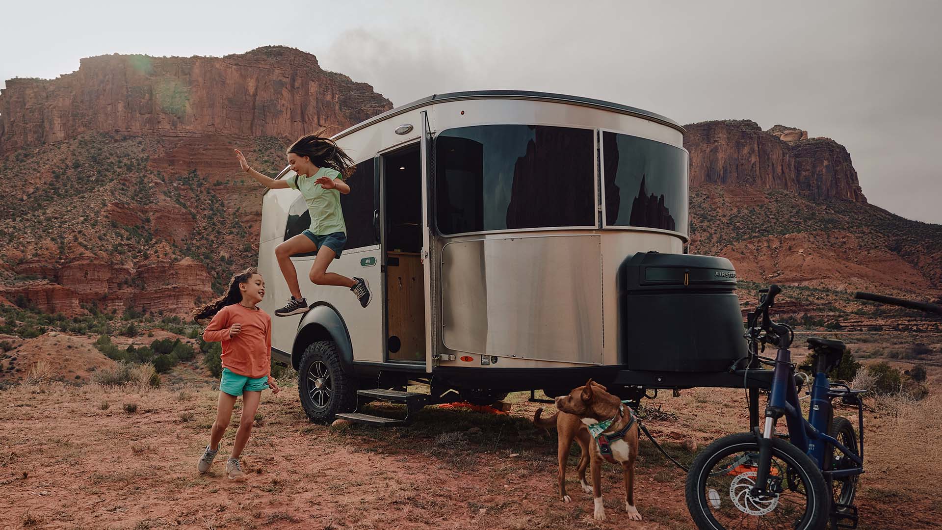 Airstream Basecamp at a red-rock desert campsite with two children, a dog, and bicycles