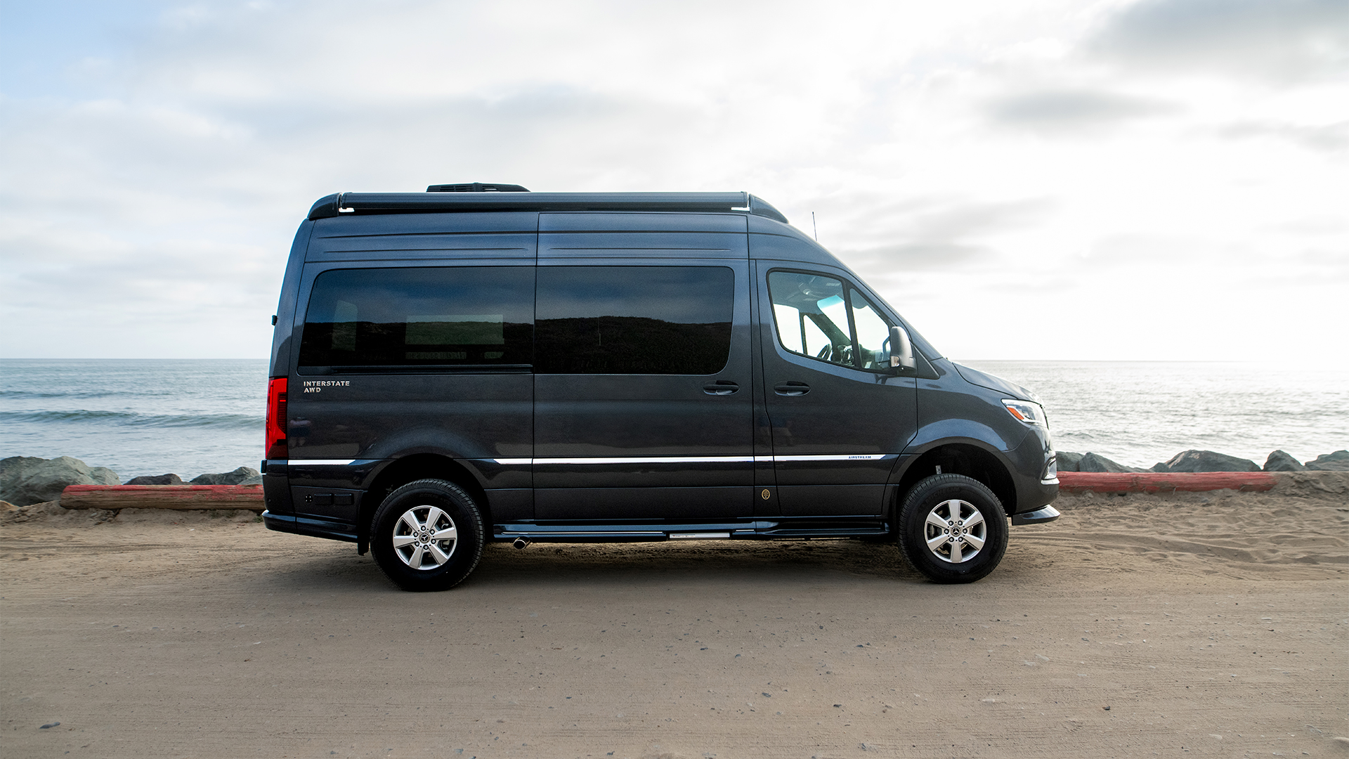 Dark Airstream Interstate 19GT touring coach parked beside the ocean