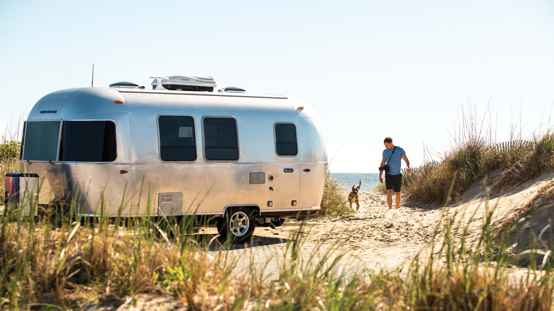 Airstream Bambi beside an adventurous traveler and dog near the coast