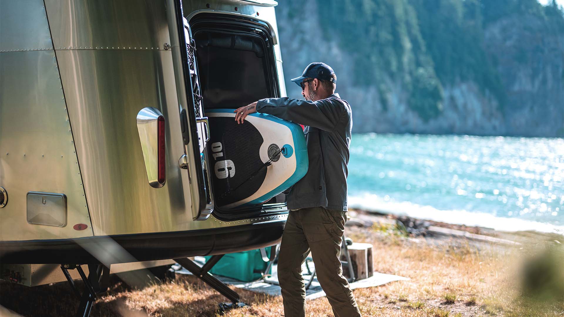 Traveler loading a paddleboard through an Airstream Basecamp rear hatch