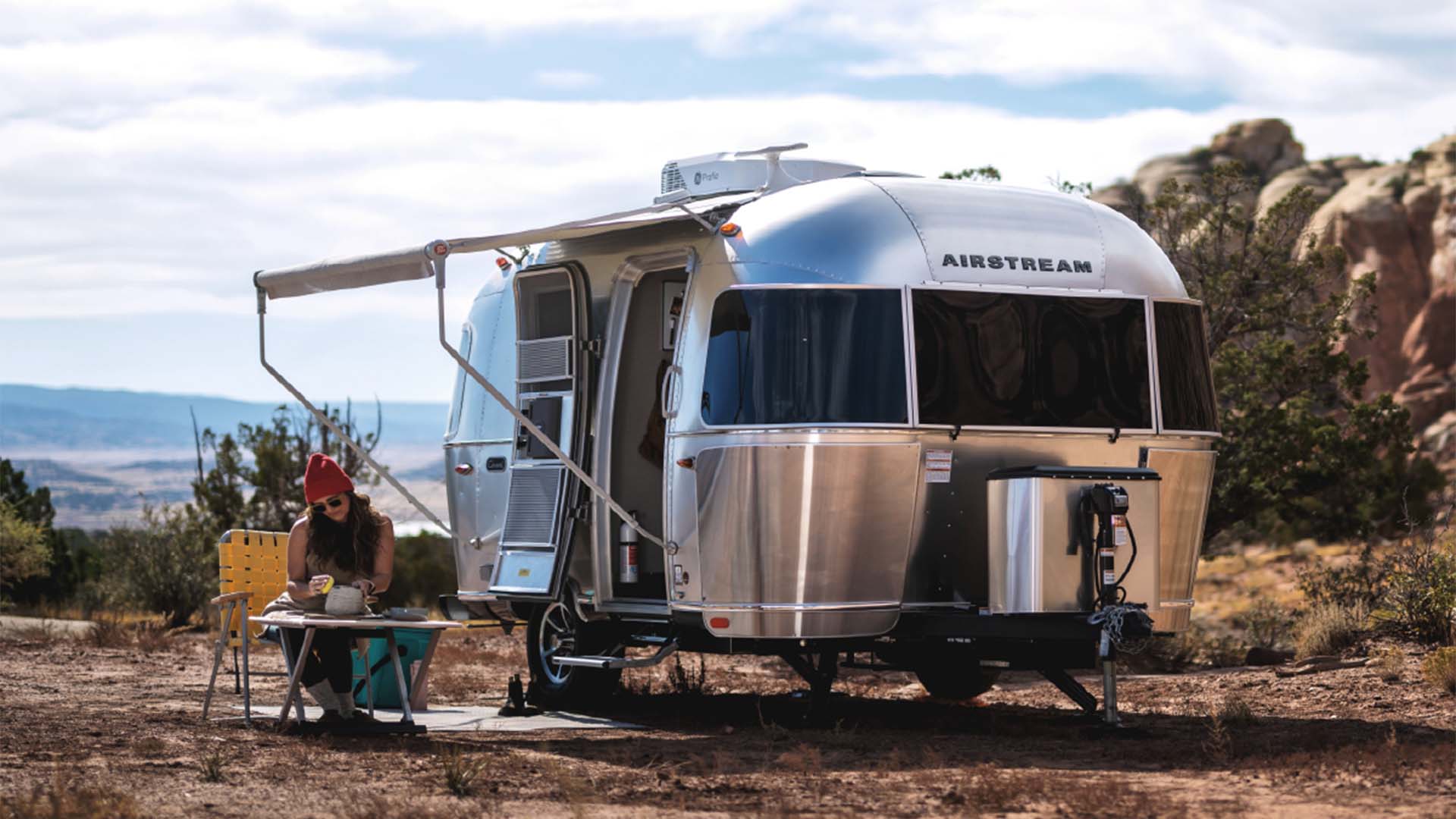 Airstream Caravel at a desert campsite with a traveler seated beneath the awning