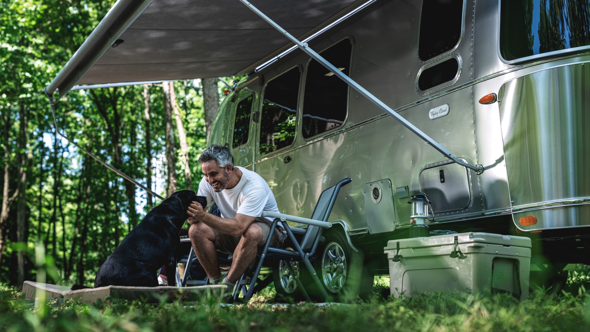 Traveler and dog relaxing beside an Airstream Flying Cloud
